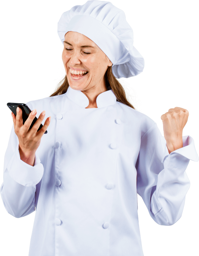 Uma cozinha. Mulher de meia idade vestida com um fardamento de cozinheira vibrando ao olhar o celular com cenário de fundo sendo uma cozinha industrial